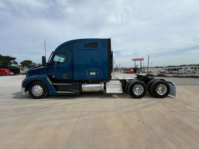 Kenworth T680 tractor in blue side view showing sleeper cab, dual rear axles, chrome fuel tanks and exhaust, side steps, daytime.