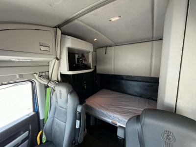Kenworth T680 sleeper cab interior with bunk bed, overhead cabinets, and a small window; driver seat and passenger seat visible; light gray interior.