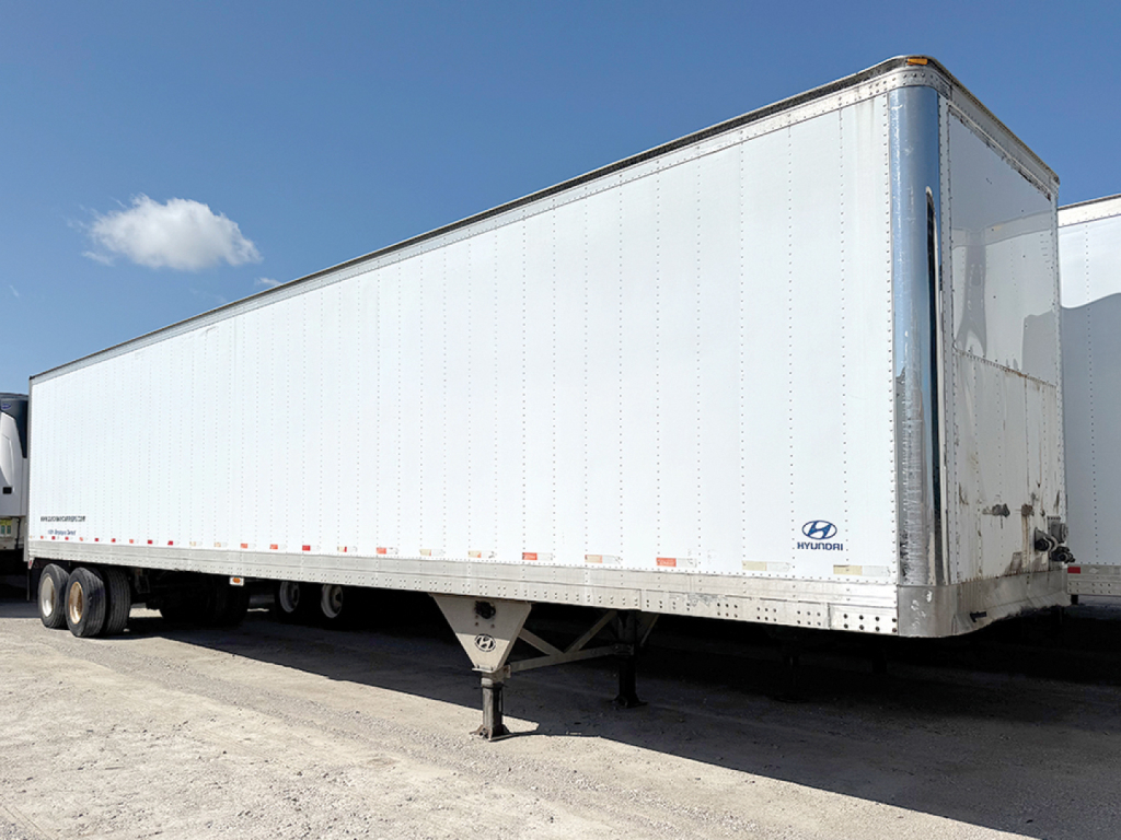 Trailer side view showing Hyundai aluminum reefer trailer with white exterior and blue Hyundai logo near front corner.