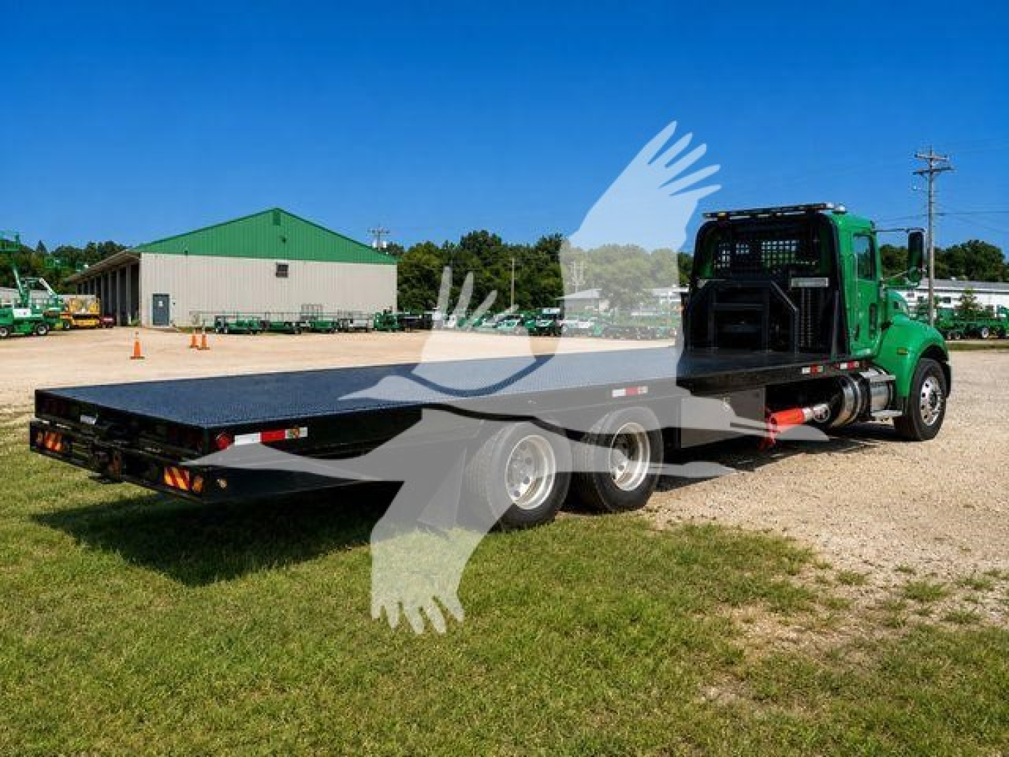 Peterbilt 348 rollback truck with flatbed, green cab, three rear axles, parked on grass and gravel.