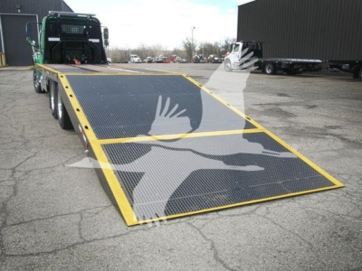 Peterbilt 348 rollback truck with lowered ramp flatbed, showing black speckled bed surface with yellow edge trim and rear hauler in a parking lot.