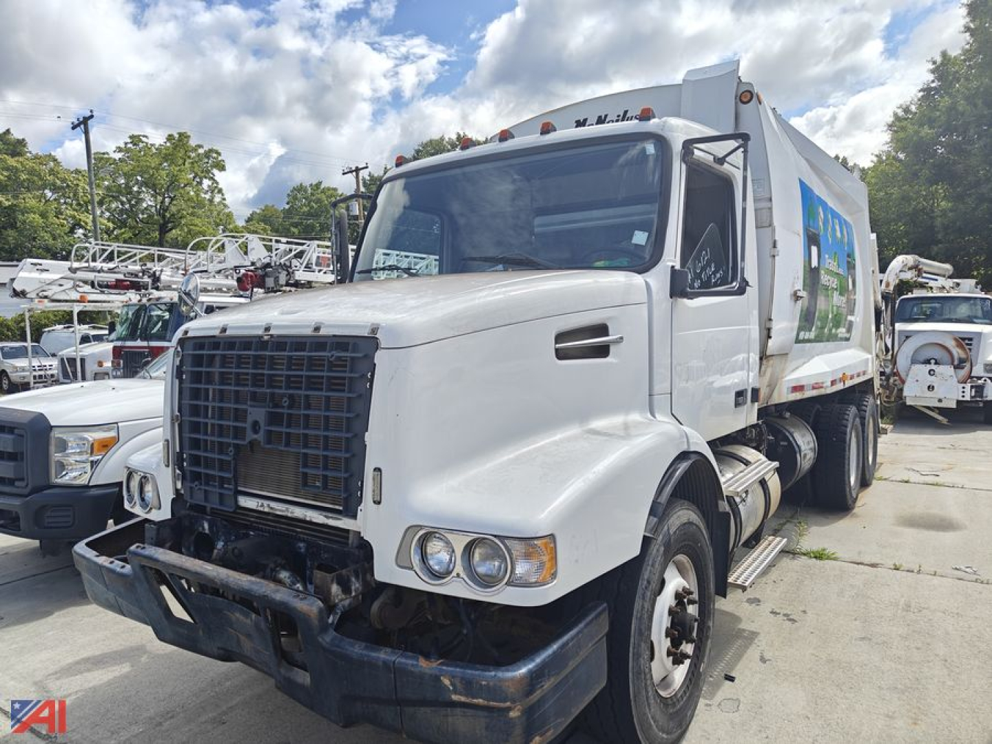 Front view of a white 2002 Volvo VHD garbage truck with a large black grille, dual round headlights, and a rear-compartment body with side graphic; AM/FM dash area visible through windshield.