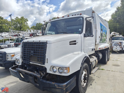 Front view of a white 2002 Volvo VHD garbage truck with a large black grille, dual round headlights, and a rear-compartment body with side graphic; AM/FM dash area visible through windshield.