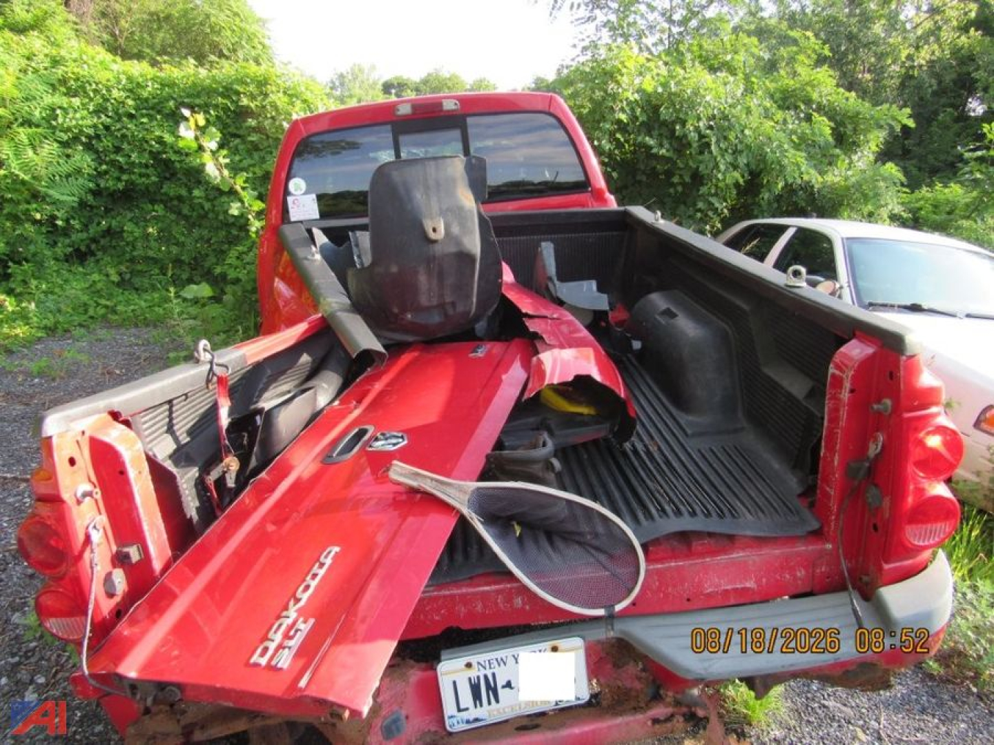 Truck bed of a red Dodge Dakota pickup showing a damaged tailgate and interior; visible debris and a black seat, with a date stamp 08/18/2026 in the lower right.