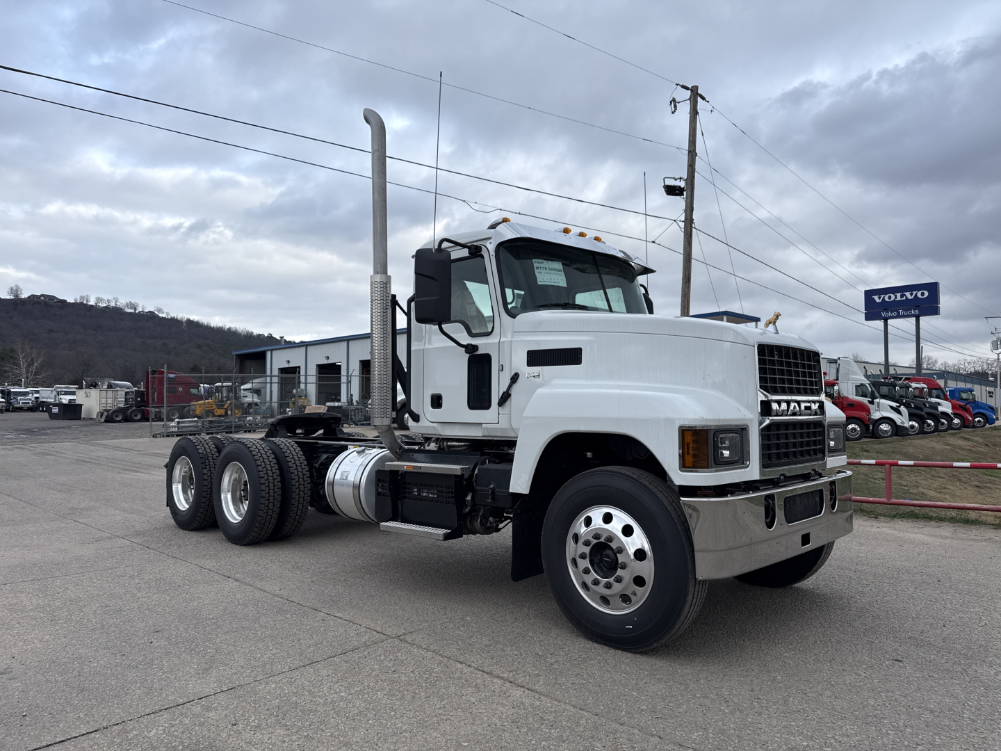 Mack PI64T conventional day cab truck in white, side view showing cab, exhaust stack, dual rear axles, 6x4 configuration, no trailer, dealership lot in background.