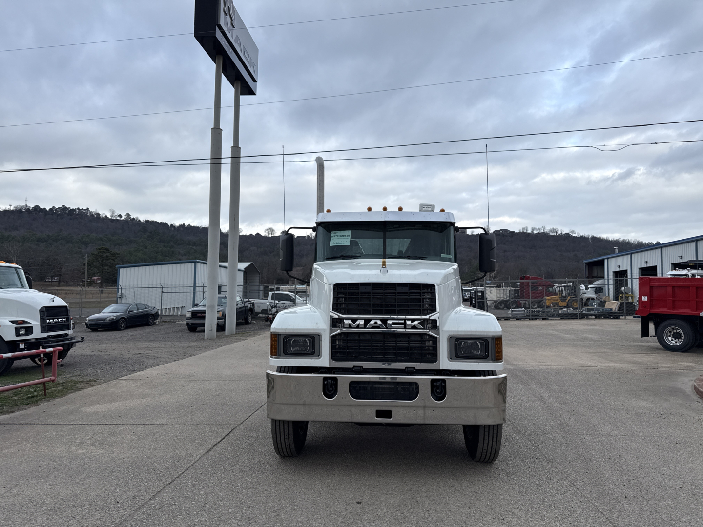 Truck front view of a white Mack PI64T conventional daycab showing front grille with MAC K lettering and bumper, in a dealership lot.