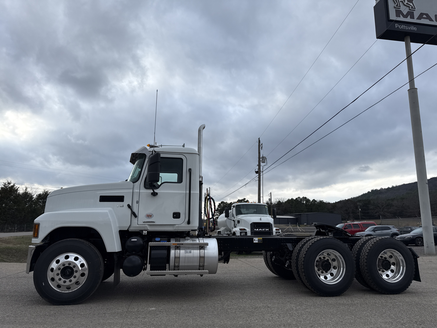 Truck chassis of a 2026 Mack PI64T conventional daycab showing front left profile, fuel tanks, dual rear axles, and wheels.