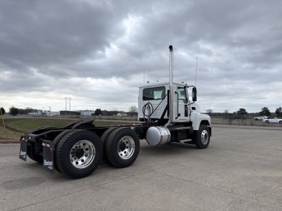 Conventional daycab truck shows a white 2026 Mack PI64T with a large vertical exhaust stack, two-axle rear and single front axle, in an open lot.