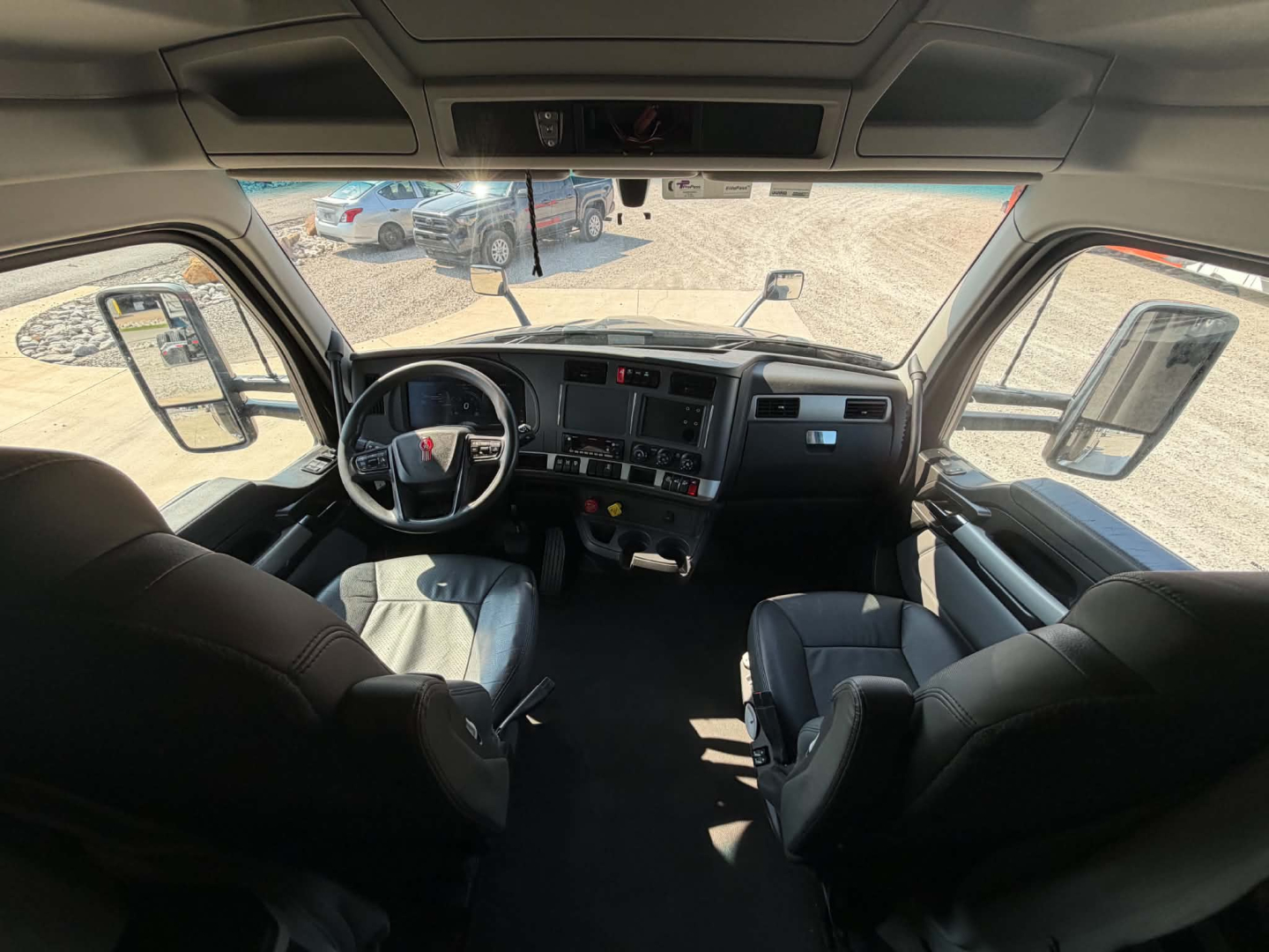 Cab interior of a 2023 Kenworth T680 with steering wheel, dashboard, and seating. Visible text includes none clearly legible except general truck cockpit features.