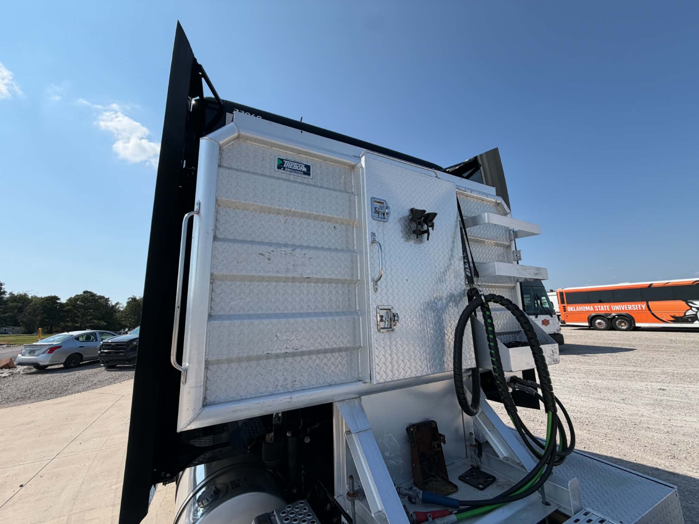 Kenworth T680 sleeper cab in a loading yard showing a diamond plate dump bed with hydraulic hoses and metal panels.