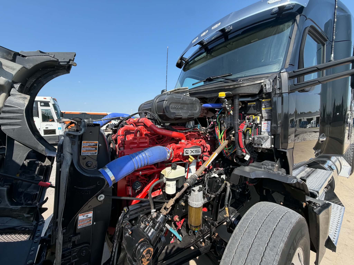 Kenworth T680 engine bay showing large red engine with blue intercooler hose and various hoses and wiring under open hood.
