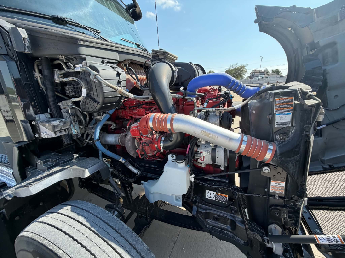 Kenworth T680 engine bay with red engine, blue silicone hoses, black radiator fan shroud, and metal tubing visible.