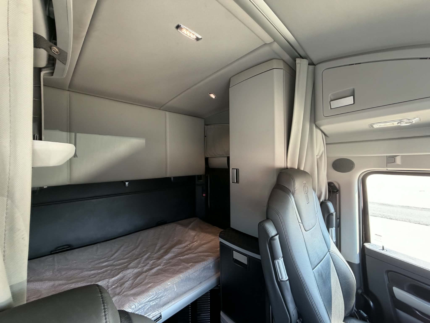 Kenworth T680 sleeper cab interior showing upper bunk, side cabinets, and driver's seat with light gray trim.