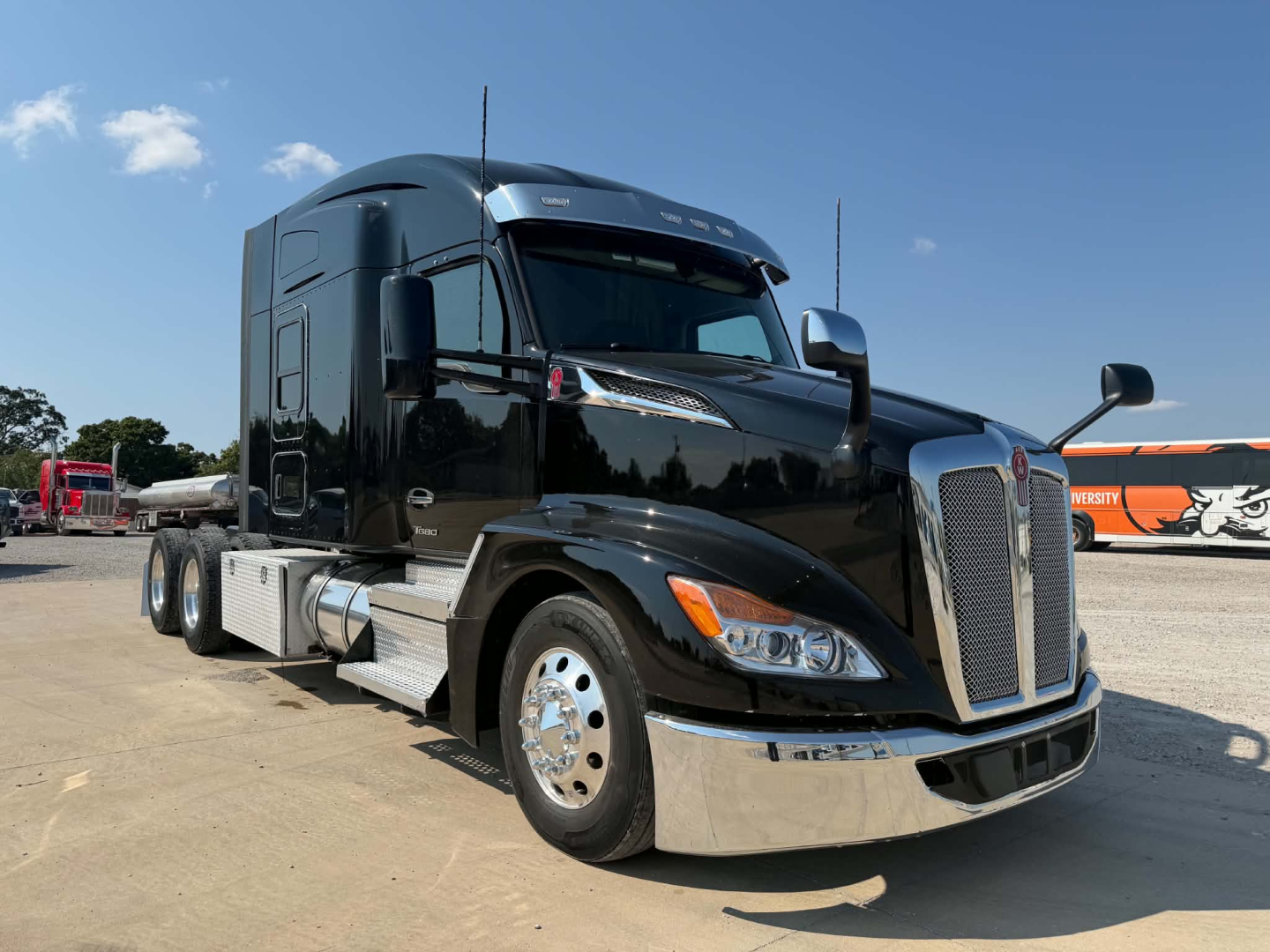 Kenworth T680 truck in a parking lot showing front chrome grille, black cab, and side fuel tanks. Visible text on badge area and mirrors.