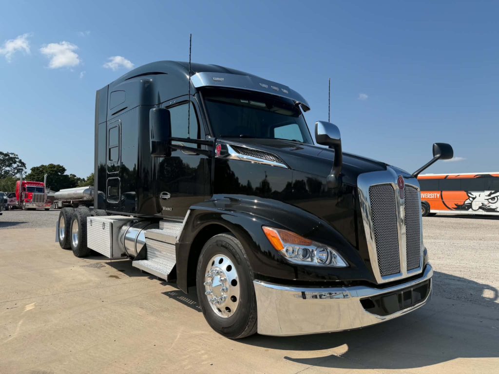 Kenworth T680 truck in a parking lot showing front chrome grille, black cab, and side fuel tanks. Visible text on badge area and mirrors.