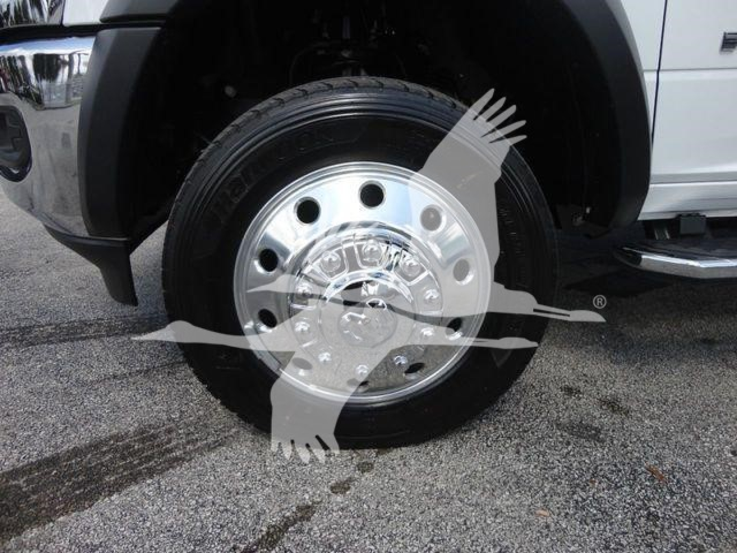 Wheel/rim close-up on a Ram 5500 truck front showing polished chrome hubcap and tire; part of front fender and step/side rail visible.