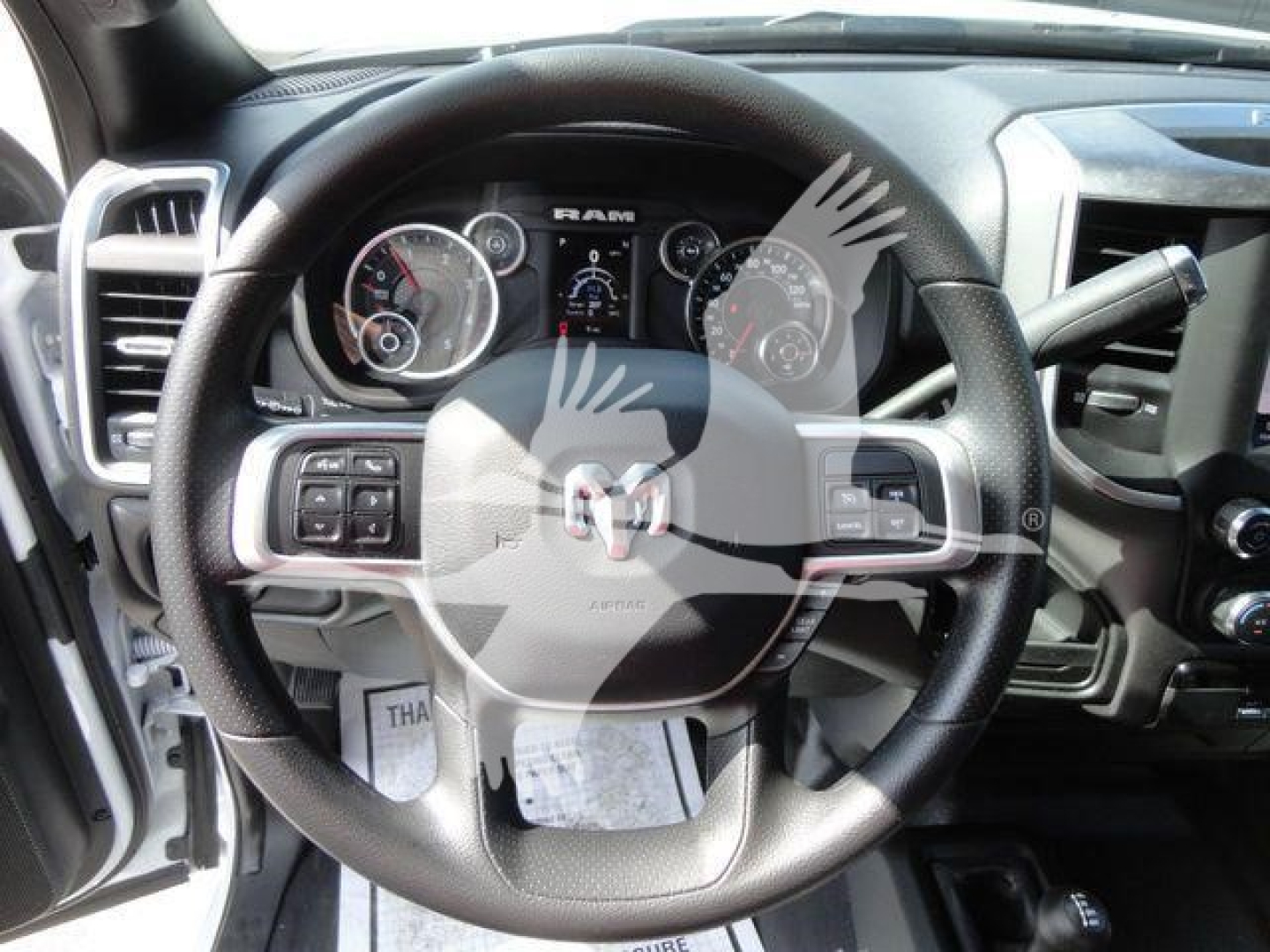 Ram steering wheel and dashboard in a pickup truck cabin with instrument cluster showing gauges, RAM logo on center, and controls on steering wheel.