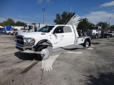Ram 5500 tow truck with white cab and flatbed, front grille and dual rear wheels visible, dealership lot in background.