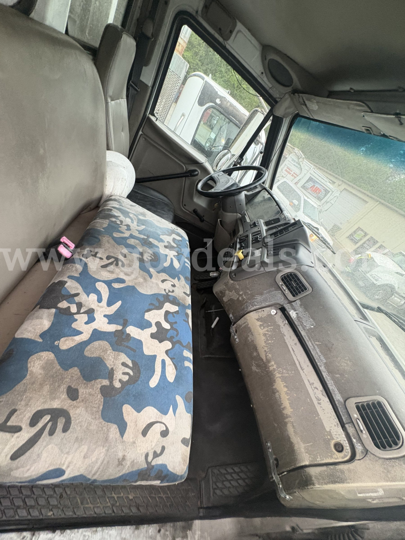 Cab interior of a Sterling LT8500 front section showing steering wheel, dashboard with gauges, and seat upholstery; dusty cabin with fabric bench seat and camouflage pattern.