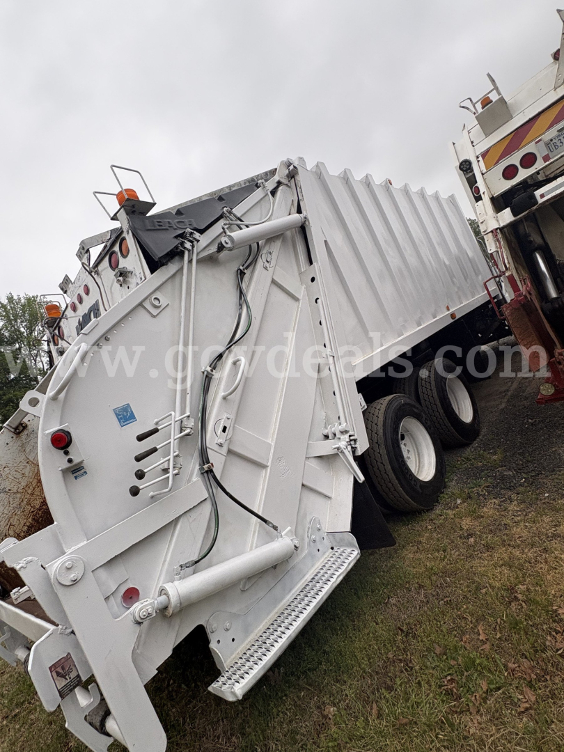 Dump truck hopper trailer showing hydraulic hoses and access steps with white metal body.