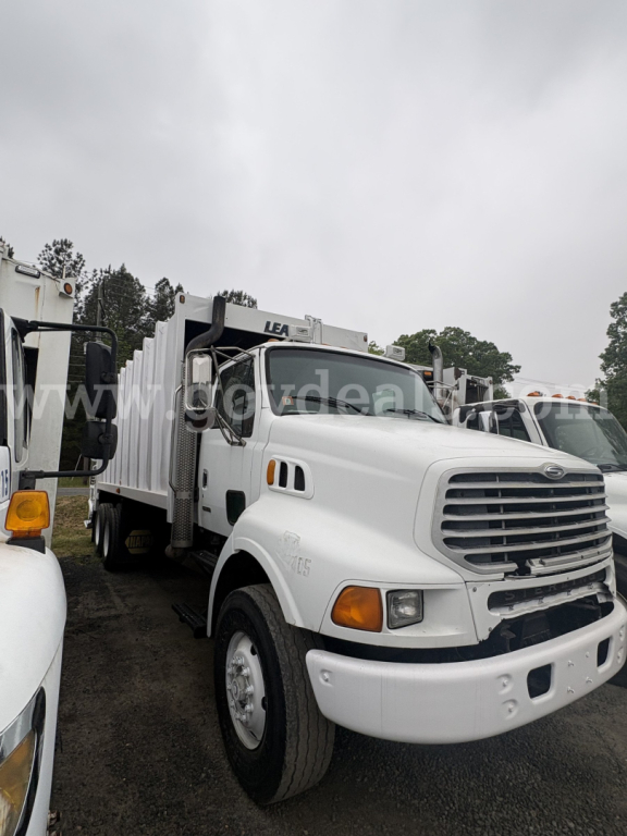Truck front view showing white Sterling LT8500 cab with large grille, headlights, and turn signals; utility body on chassis; overcast sky.