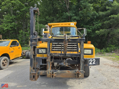 Front view of a yellow Mack RD690P dump truck with a heavy equipment attachment in the loader frame, number 22 plate, in a gravel lot.