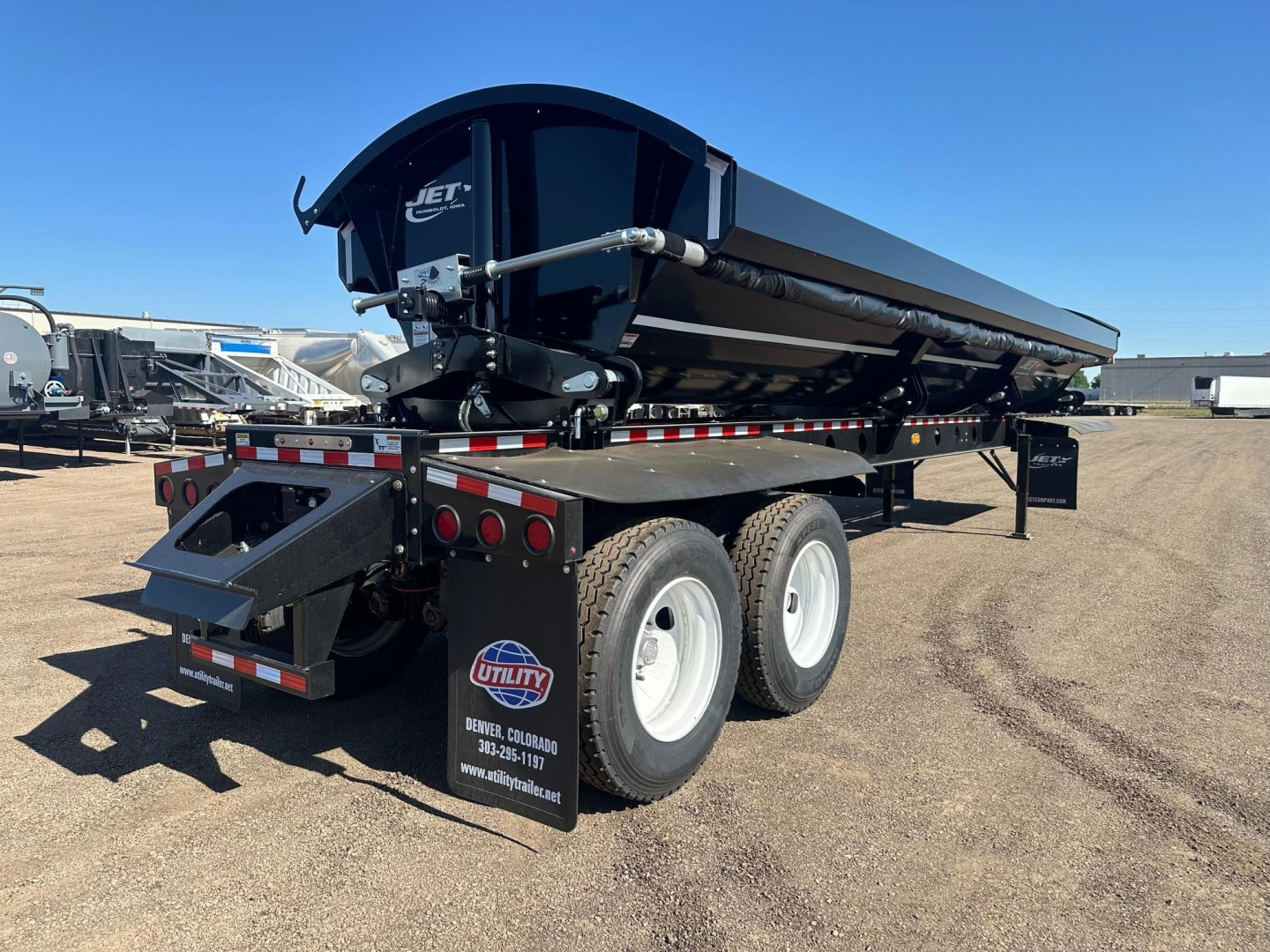 Jet Jet side dump trailer showing large black dump body on triple-axle with white wheels, rear tailgate and reflective tape