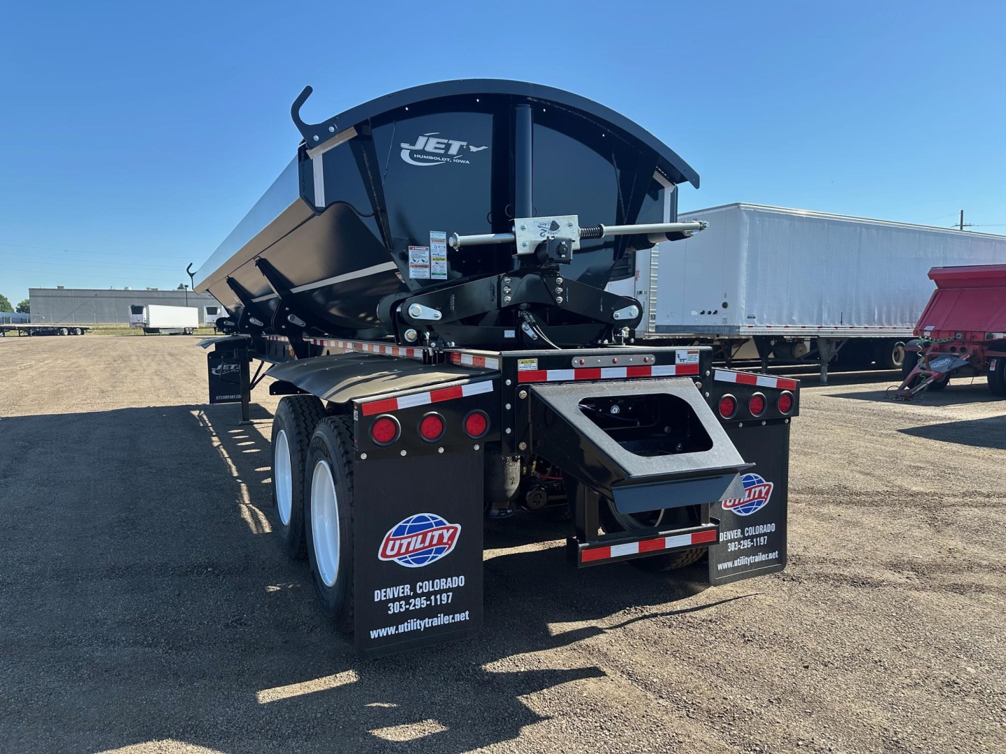 Jet brand side-dump trailer rear view showing tires, mud flaps, and hydraulic mechanism with Jet logo on round hopper.