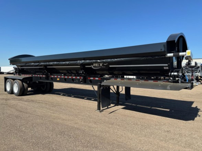 Jet side dump trailer shown in profile with black exterior, tandem axles, and support legs under a long flatbed. Visible branding 'JET' on the side near the center, with storage context around.