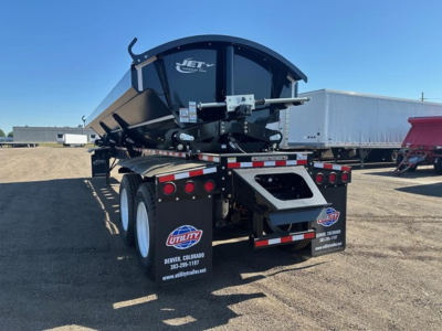 Jet side dump trailer rear view showing black dump body with Jet logo and dual rear axles, deck and hydraulic mechanism visible.
