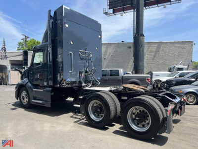 Volvo VNL day cab tractor in a parking lot, side view showing rear axles and chassis with fifth wheel, blue cab, and black chassis.