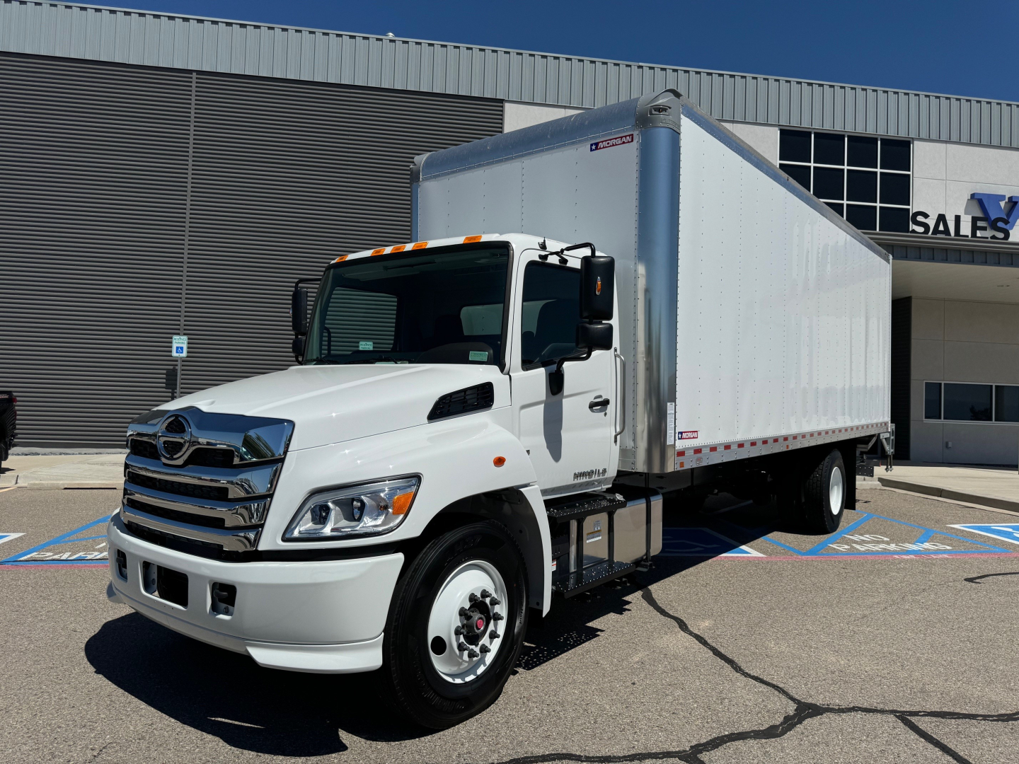 Hino L6 box truck in showroom lot showing cab and white cargo box with chrome front grille and headlights.