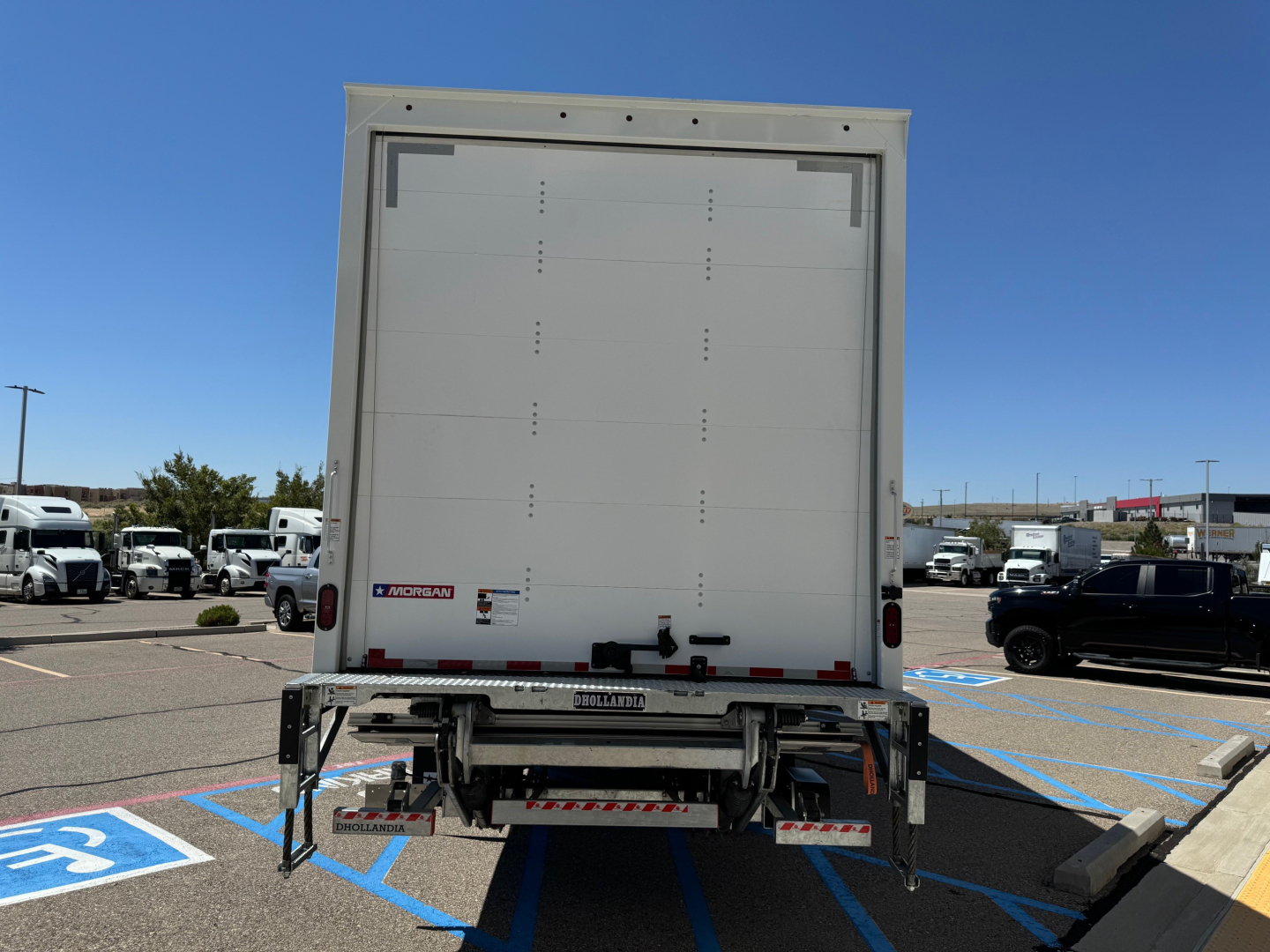 Box truck rear view showing liftgate and rear doors with Mogensen/Hyundai-style logo and stickers.