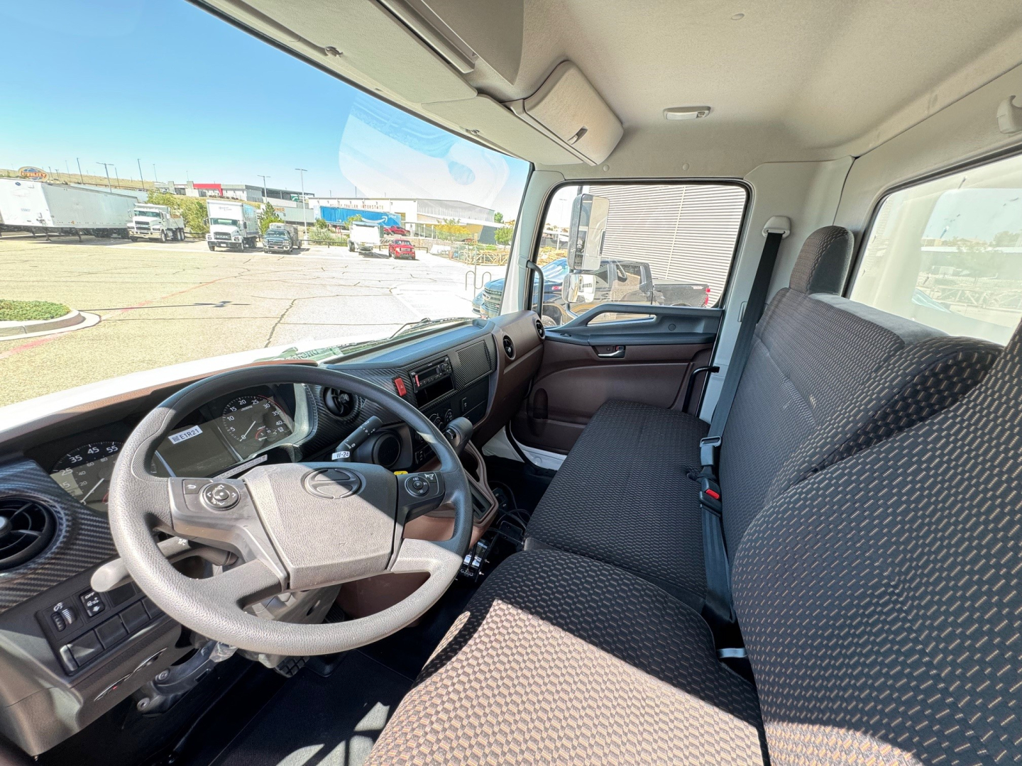 Truck cabin interior with steering wheel and front bench seat, dashboard showing gauges and controls, driver and passenger seats in fabric.