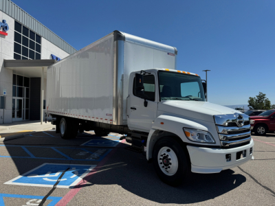 Box truck with white cab and large cargo box parked at dealership lot.