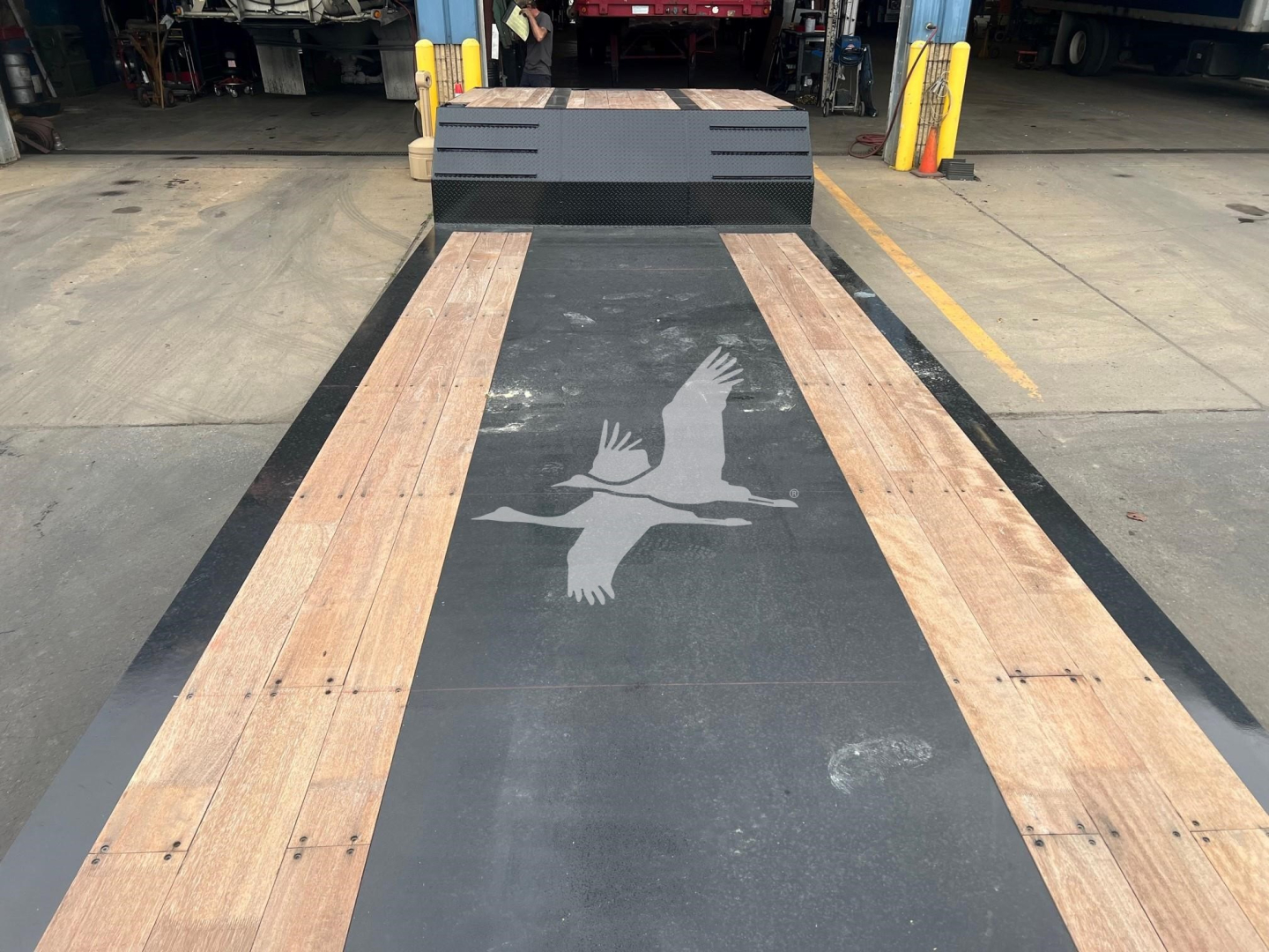 Trailer bed of XL Specialized Mini Deck showing wood planks on steel deck with logo, and entry step in background.