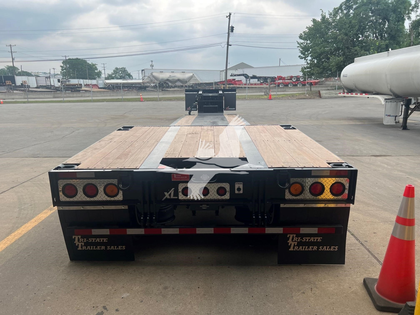 Trailer rear view of a 2025 XL Specialized Mini Deck, double drop expandable trailer in a parking lot showing taillights, mud flaps labeled 'THE-STATE TRAILER SALES' and wooden deck.