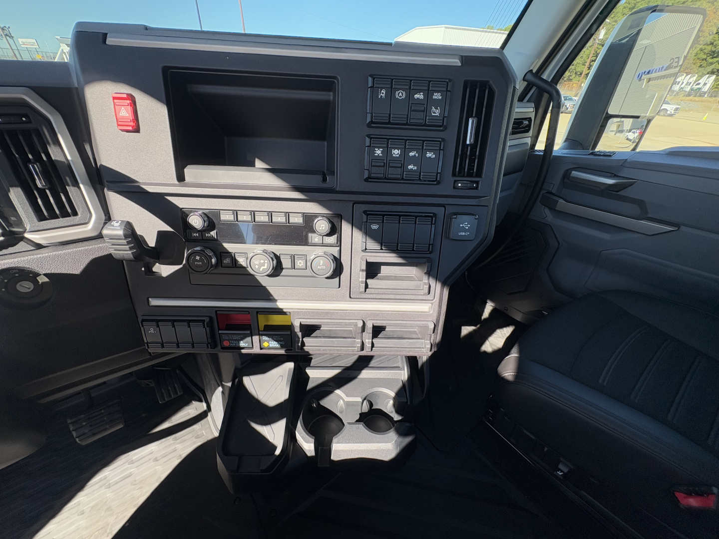 Dashboard area of a 2026 Mack PR64T truck showing instrument cluster controls, switches, and storage compartments.