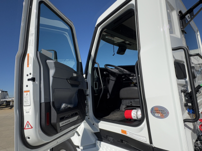 Mack PR64T cab interior view with open door showing steering wheel, dashboard, and driver's seat.