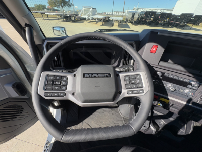 Mack PR64T truck interior view showing steering wheel with Mack logo and control controls on both sides, dashboard and center stack visible.