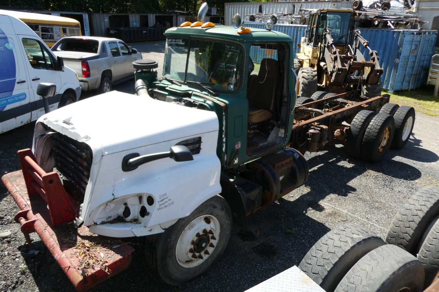 Cab and chassis truck showing green cab and white front with red bumper guard, attached to a long flatbed trailer frame and various equipment on the back.