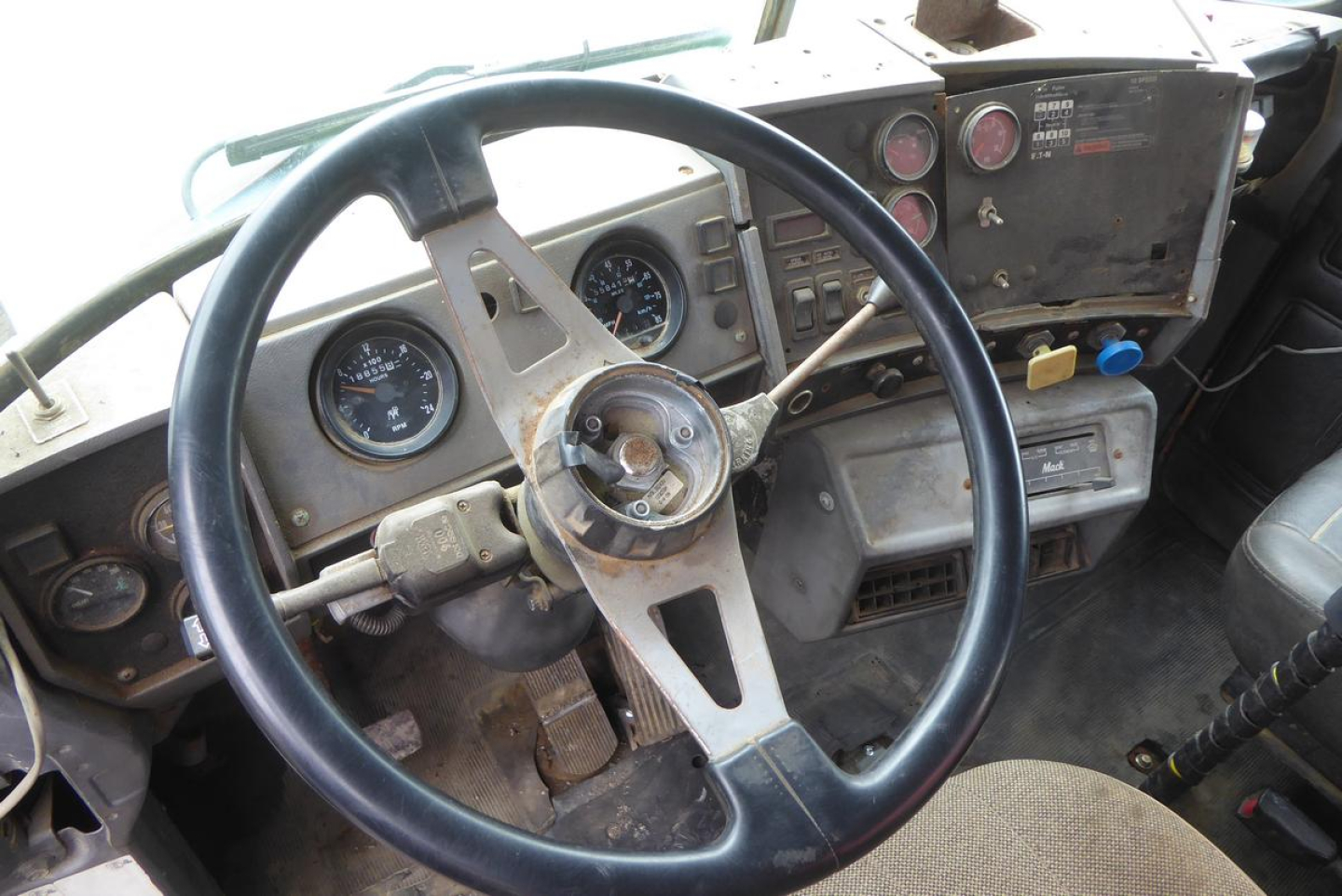 Mack RD688S dash and steering wheel showing gauges and old instrument cluster. Steering wheel with three spokes, circular speedometer, and control panel with switches.