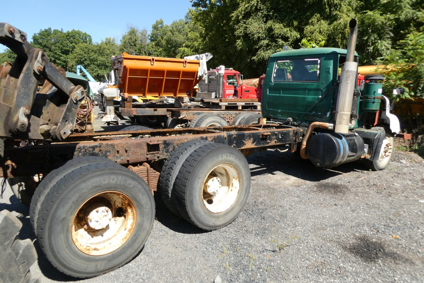 Mack RD688S truck chassis showing removed bed, with green cab on the right and a flatbed/wheeled trailer behind. Visible tires and rust on rims.