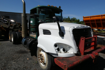 Mack RD688S cab and chassis with white front fender, green cab, red front bumper, exposed headlights and grille area, on a gravel lot.