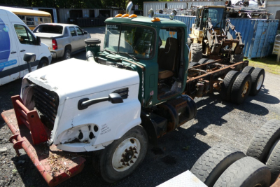 Cab and chassis truck showing green cab and white front with red bumper guard, attached to a long flatbed trailer frame and various equipment on the back.