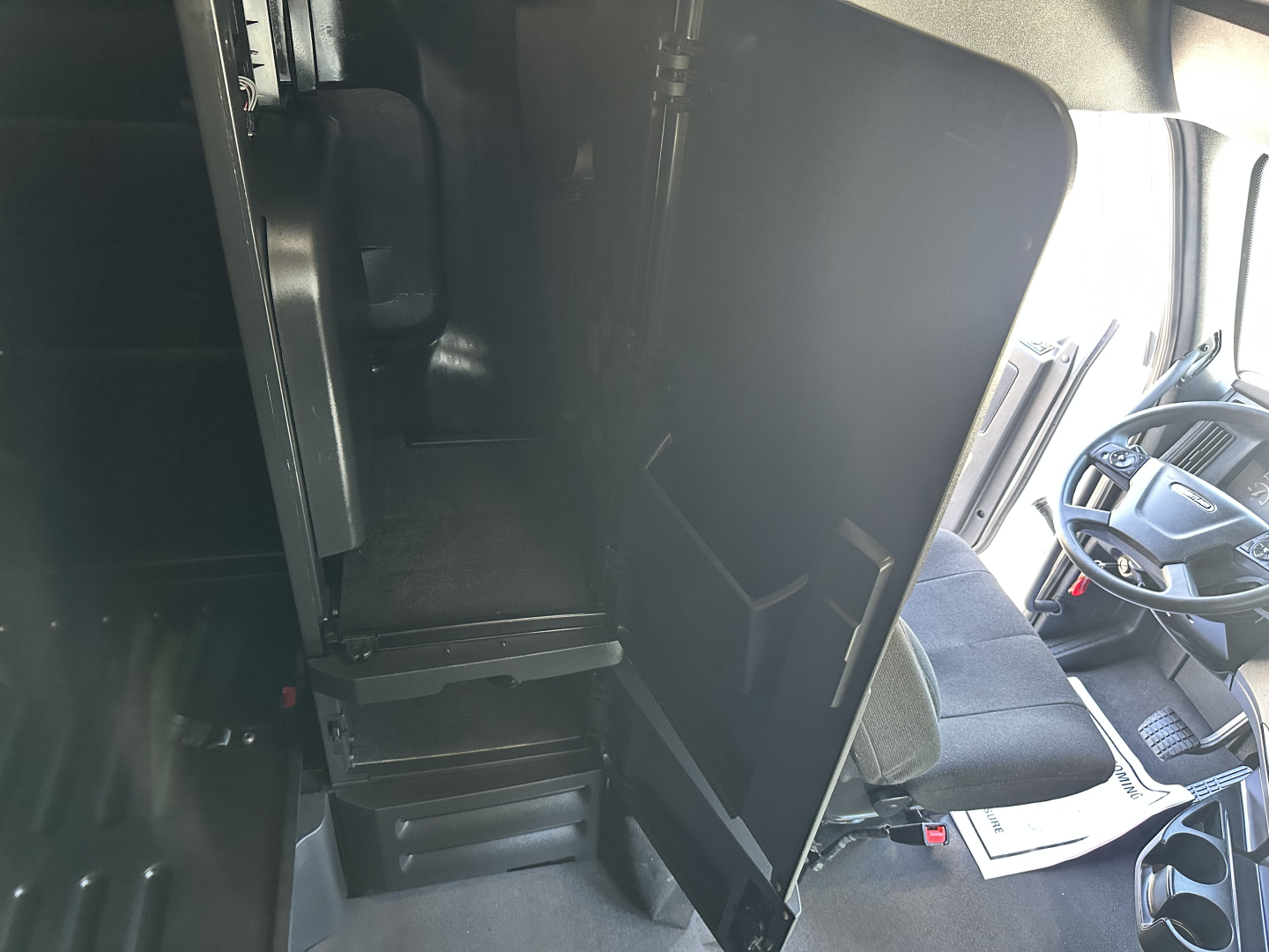 Cab interior of a Freightliner Cascadia 126 showing driver seat, dashboard, and open partition or sleeper area with step-down access to cab interior.