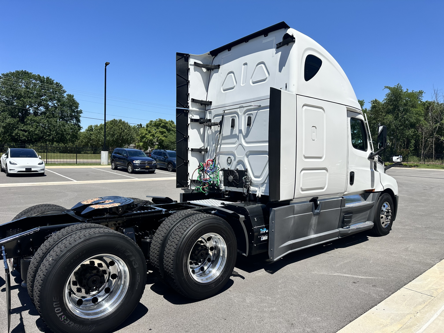Freightliner Cascadia 126 sleeper tractor in a parking lot, side view showing rear wheels and cab with raised roof, no visible text on decals.