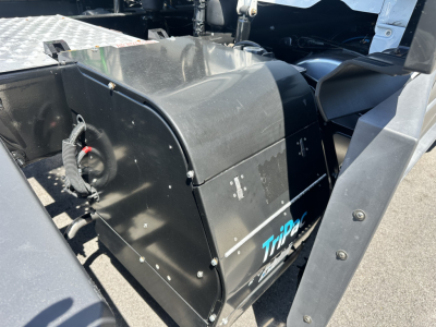 Tractor-trailer cab interior view showing engine bay area with large black battery box labeled Tripal or Tripa? and cables; Freightliner Cascadia 126 cabin region visible.