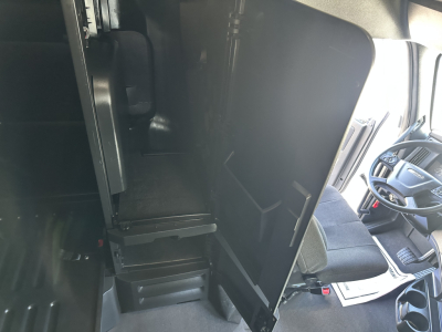 Cab interior of a Freightliner Cascadia 126 showing driver seat, dashboard, and open partition or sleeper area with step-down access to cab interior.