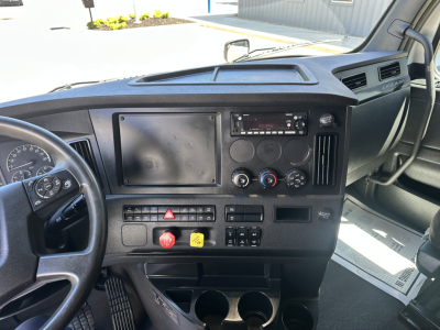 Truck interior dashboard of a 2023 Freightliner Cascadia 126 viewed from the driver's seat showing steering wheel, instrument cluster, center console with blank panel, climate controls, radio, hazard switch, and cup holders.